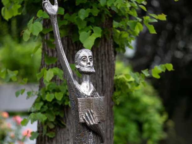Metallskulptur „Der Prophet“ mit erhobenem Arm vor grünem Laub in Wipperfürth