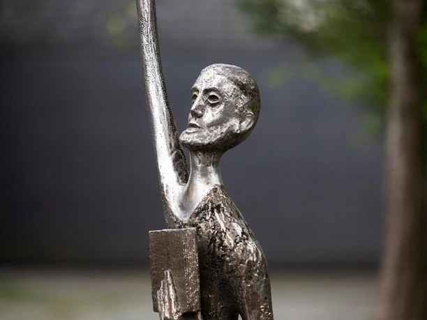 Bronzeskulptur Der Prophet mit erhobenem Arm und Buch vor unscharfem Hintergrund