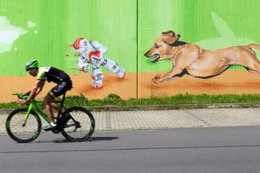 Radfahrer vor grüner Wand mit Graffiti: Roboter und Hund im schnellen Lauf