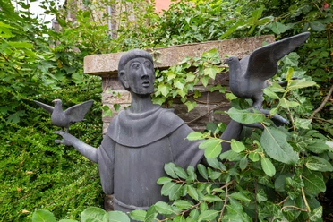 Statue des heiligen Franziskus mit zwei Vögeln zwischen dichtem Grün in Wipperfürth