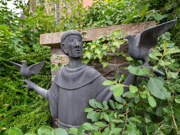 Statue des heiligen Franziskus mit zwei Vögeln zwischen dichtem Grün in Wipperfürth