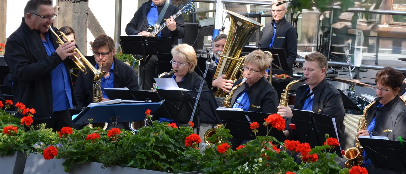 Das Orchester SoundWerk spielt im Rosengarten vor roten Geranien.