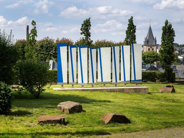 Blaue und weiße Ort-und-Zeit-Tafeln in Grünanlage mit Kirchturm im Hintergrund