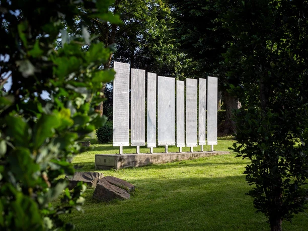 Helle Ort-und-Zeit-Tafeln von Daphna Koll zwischen Bäumen auf einer Wiese