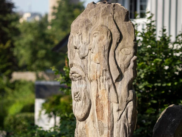 Steinskulptur „Zeitschienen“ auf Gleisstücken, im Hintergrund die Kirche von Wipperfürth