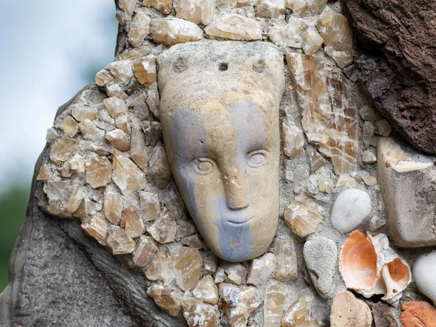 Steinernes Gesicht in einer Skulptur, umgeben von Kristallen, Muscheln und Kieseln