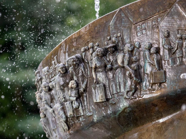 Nahaufnahme des Brunnendenkmals mit Wasserstrahl und bronzenen Relief-Figuren