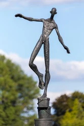 Dunkle Figurenskulptur balanciert mit ausgestreckten Armen auf gestapelten Eimern