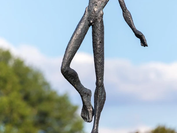 Dunkle Figurenskulptur balanciert mit ausgestreckten Armen auf gestapelten Eimern
