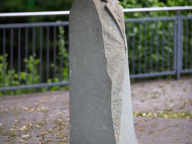 Steinskulptur Fritz Hamel mit Mütze und Mantel vor Geländer im Grünen