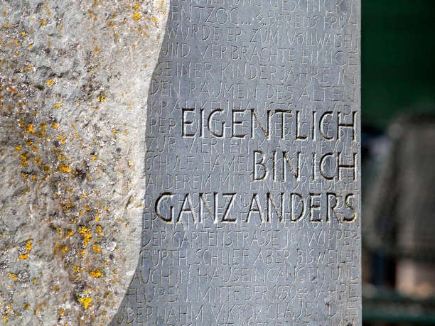 Nahaufnahme einer beschrifteten Steintafel der Fritz-Hamel-Skulptur neben Flechten.