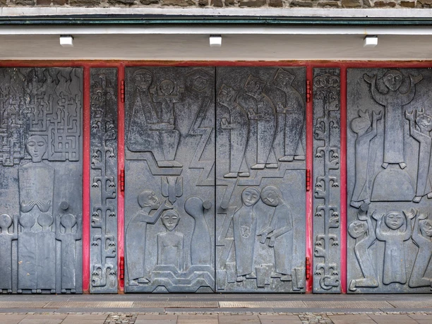 Kirchenportal von Toni Zenz mit grauen Reliefs und roten Rahmen in Marienheide