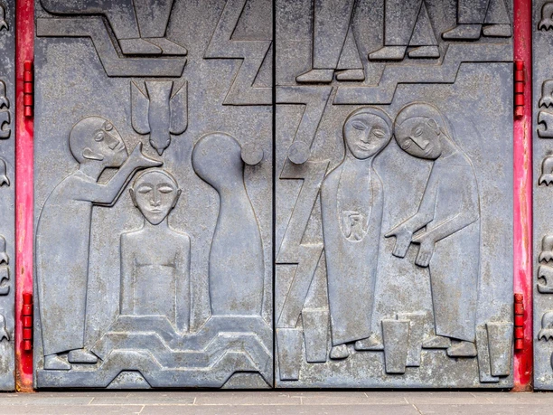 Relief am Kirchenportal von Toni Zenz mit stilisierten Figuren und roten Türbändern