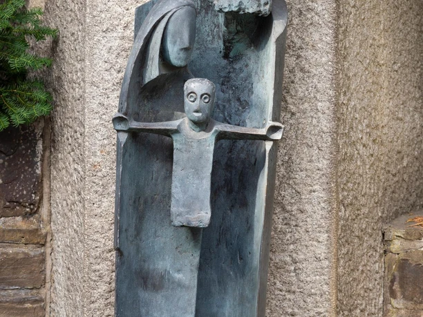 Bronzeskulptur Klausner Heinrich mit Kind vor rauer Steinwand in Marienheide