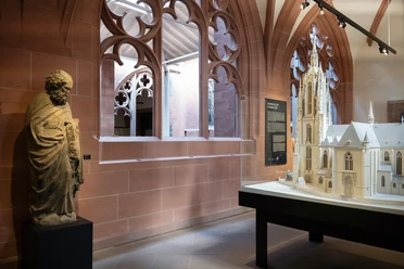 Exhibition at the Frankfurt Cathedral Museum featuring a statue, a model of the cathedral, and Gothic tracery windows