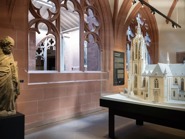 Exhibition at the Frankfurt Cathedral Museum featuring a statue, a model of the cathedral, and Gothic tracery windows