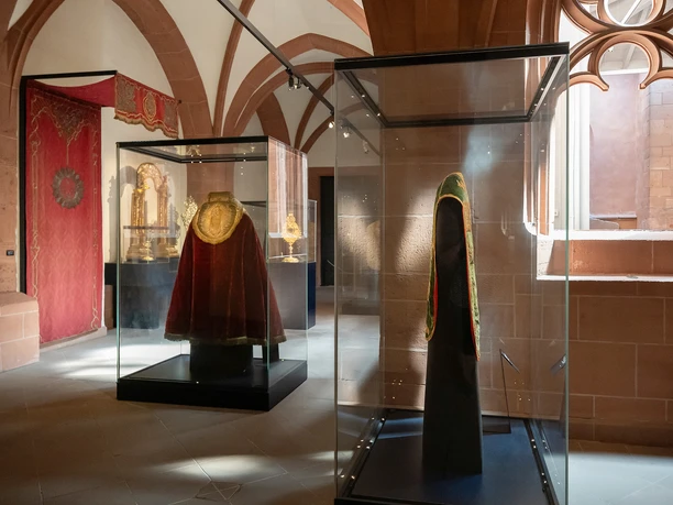 Display cases containing liturgical vestments in the Cathedral Museum beneath Gothic vaults