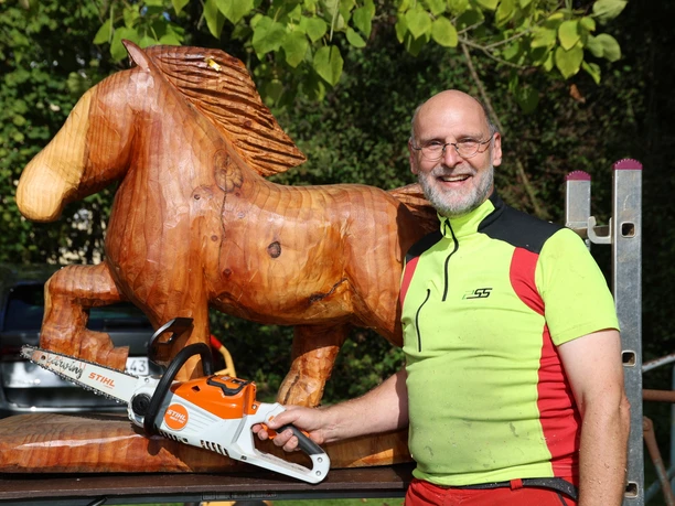 Holzkünstler mit Motorsäge neben geschnitztem Pferd beim Herbstmarkt