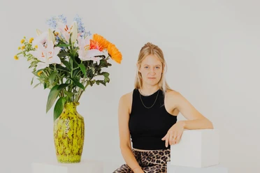 Portraitfoto der Autorin vor hellem Hintergrund neben einem großen Blumenstrauß