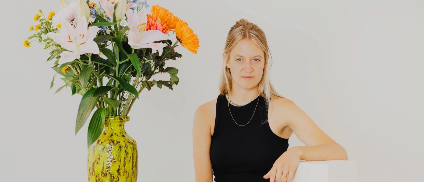 Portraitfoto der Autorin vor hellem Hintergrund neben einem großen Blumenstrauß