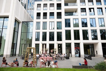 The outdoor terrace of the TOWER MMK in front of a light-colored high-rise facade featuring a golden sculpture