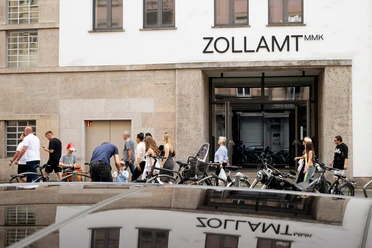Fassade des ZOLLAMT MMK in Frankfurt mit Eingang, Passanten, Fahrrädern und Spiegelung
