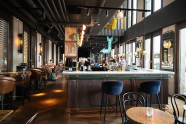 Innenraum der Ruby Louise Bar mit langer Theke, großen Fenstern und warmem Licht