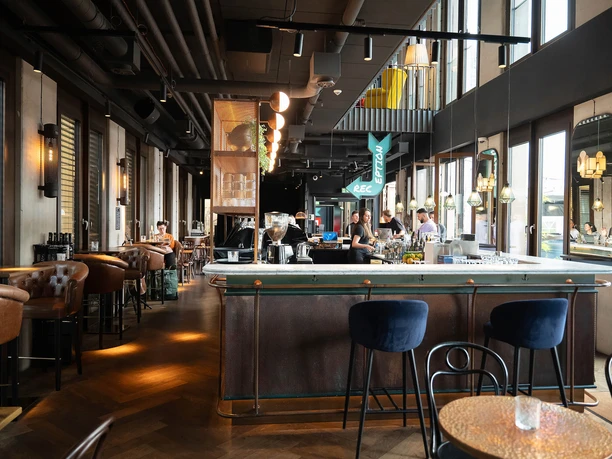 Innenraum der Ruby Louise Bar mit langer Theke, großen Fenstern und warmem Licht