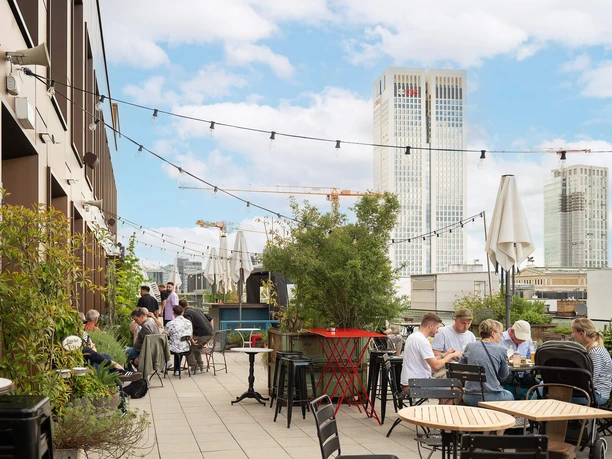 Dachterrasse der Ruby Louise Bar mit Gästen, Pflanzen und Blick auf Hochhäuser in Frankfurt