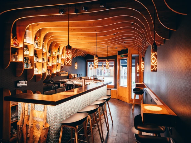 Wood-paneled bar with illuminated shelves, stools, and warm, glowing pendant lights