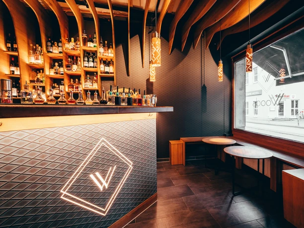 Interior of the Woods Bar, featuring an illuminated bar, a wooden ceiling, and a window facing the street