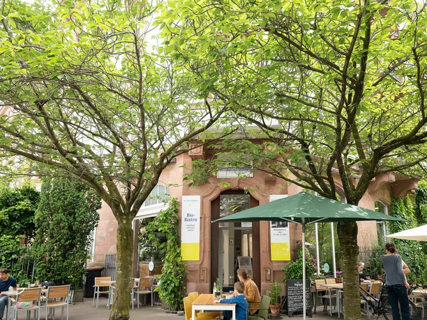 Frankfurt - Bio-Bistro Sachsenhausen Terrasse des Bio-Bistros Sachsenhausen mit Gästen, Sonnenschirmen und grünen Bäumen