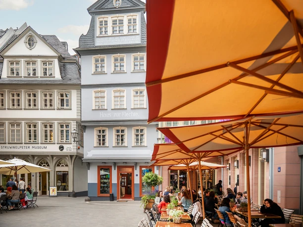 Gäste sitzen unter orangefarbenen Schirmen am Hühnermarkt vor Frankfurter Altstadthäusern