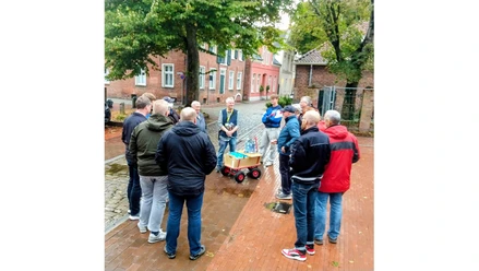 Gruppe bei einer Bierführung in der Leeraner Altstadt mit Bollerwagen auf nassem Pflaster.