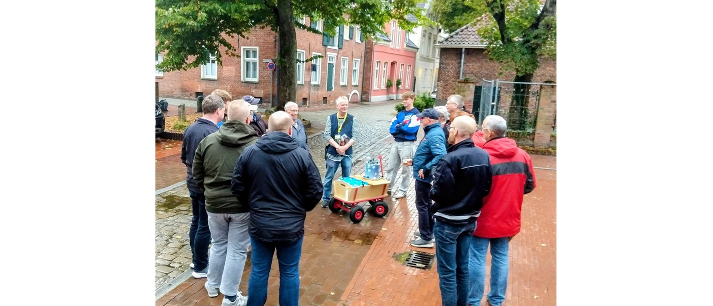 Gruppe bei einer Bierführung in der Leeraner Altstadt mit Bollerwagen auf nassem Pflaster.