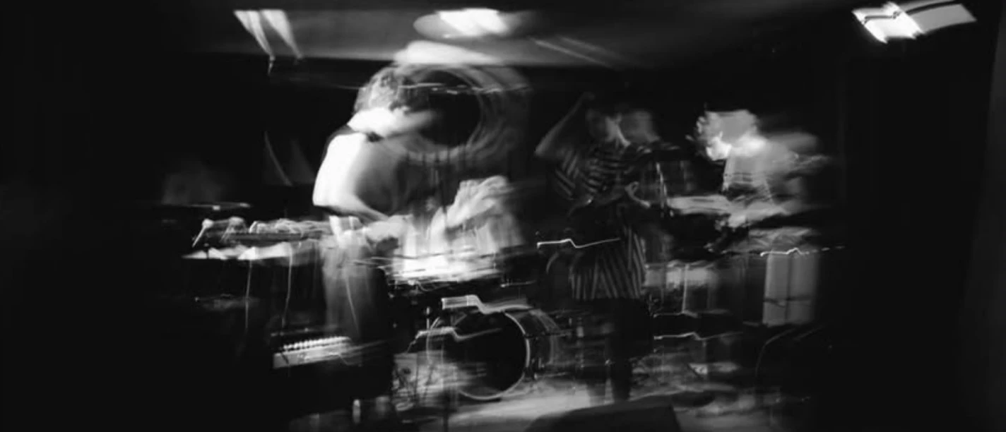 Schwarz-Weiß-Aufnahme einer Post-Punk-Band mit Bewegungsunschärfe auf dunkler Bühne