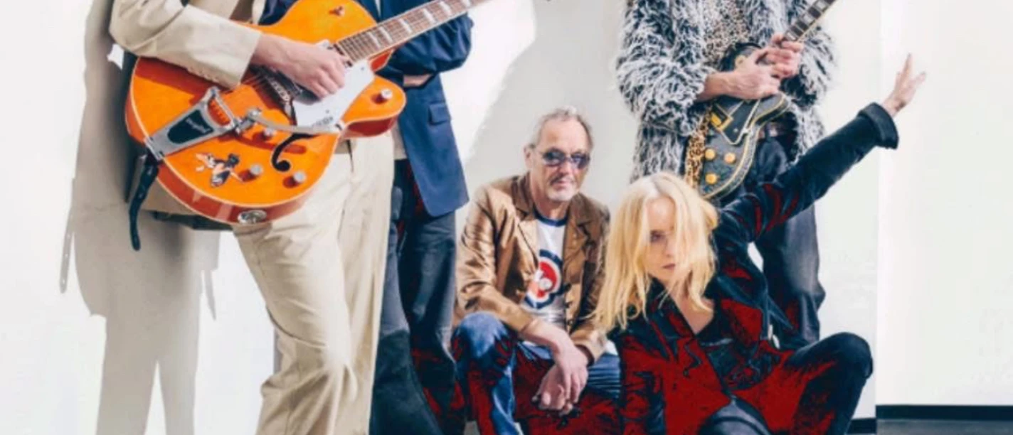 Fünfköpfige Rockband mit Sonnenbrillen und Gitarren posiert vor heller Wand