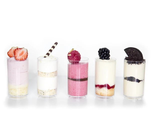 Fünf kleine Dessertgläser mit Creme, Beeren, Keks und Schokostäbchen.