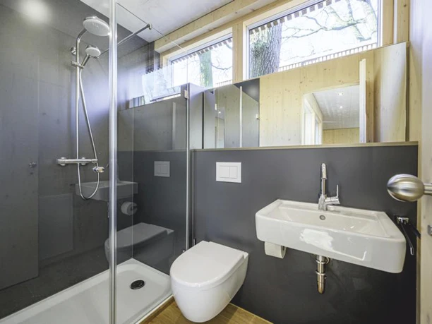 Modernes Badezimmer im Baumhaus mit Glasdusche, Toilette, Waschbecken und Holzelementen.