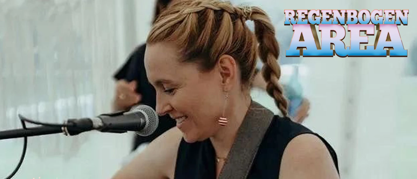 Frau mit Gitarre am Mikrofon, Text: Nina Heart, MUF '26, Regenbogen Area.