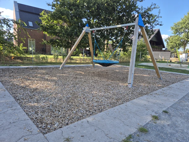 Nestschaukel auf dem Kinderspielplatz Sonnentauweg mit Bäumen und Wohnhäusern.