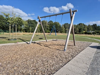 Zwei Schaukeln auf dem Spielplatz Sonnentauweg unter blauem Himmel.