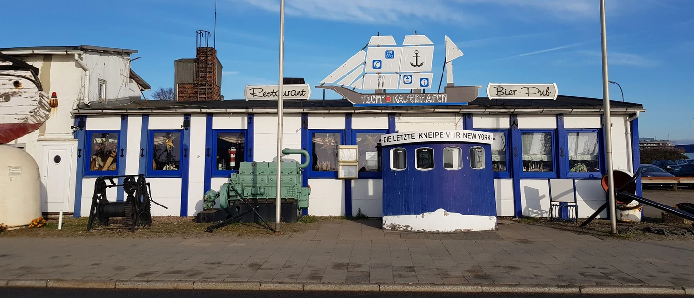 Treffpunkt Kaiserhafen mit maritimer Fassade, Flaggen und blauem Eingang.