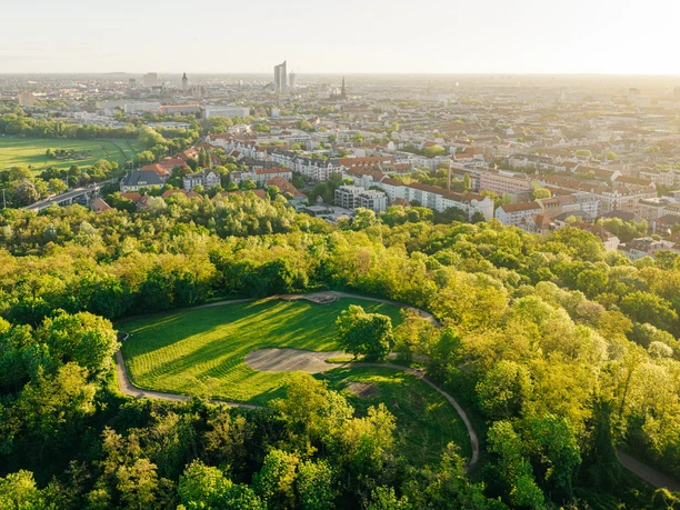 Luftaufnahme des begrünten Fockebergs mit Blick über Leipzig bei Sonnenaufgang.