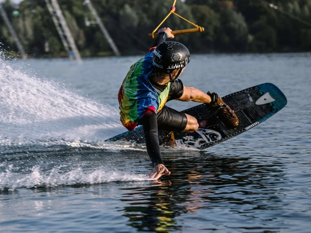 Wakeboarder zieht eine scharfe Kurve über den See und sprüht Wasser auf.