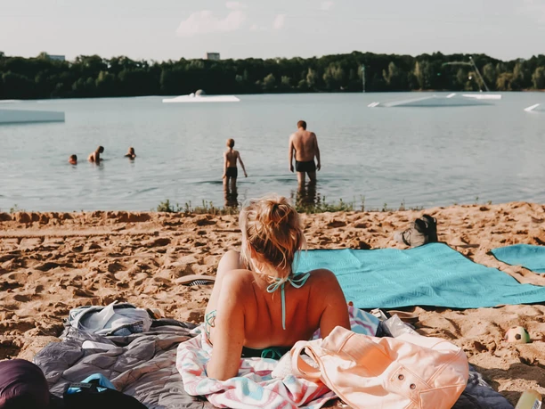 Strand am Wake Club Cologne mit Badenden im See und Wakeboard-Elementen im Hintergrund
