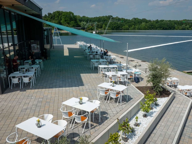 The Wake Club Cologne's lakeside terrace with tables, a sunshade, and a wakeboarding setup