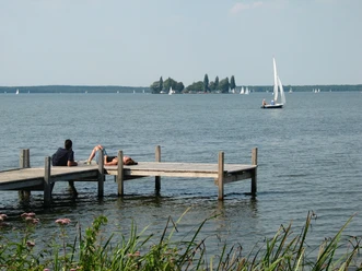 A wooden jetty juts out into the water of the Steinhuder Meer, surrounded by herbs and sailing boats on the horizon.