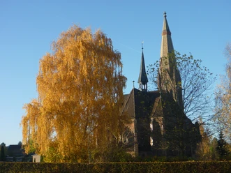 Kirche Hagenburg Kirche in Hagenburg, umgeben von herbstlich gefärbten Bäumen, unter strahlend blauem Himmel.