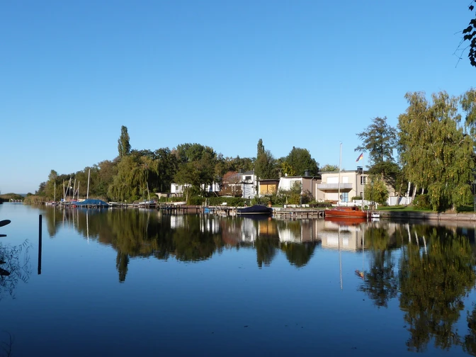 Grachten in Großenheidorn Gracht mit ruhigem Wasser, umgeben von Bäumen und Häusern im Grünen, unter klarem, blauem Himmel.Canal with calm water, surrounded by trees and green houses, under a clear blue sky.En kanal med roligt vand, omgivet af træer og grønne huse, under en klar blå himmel.Een kanaal met rustig water, omringd door bomen en groene huizen, onder een strakblauwe hemel.